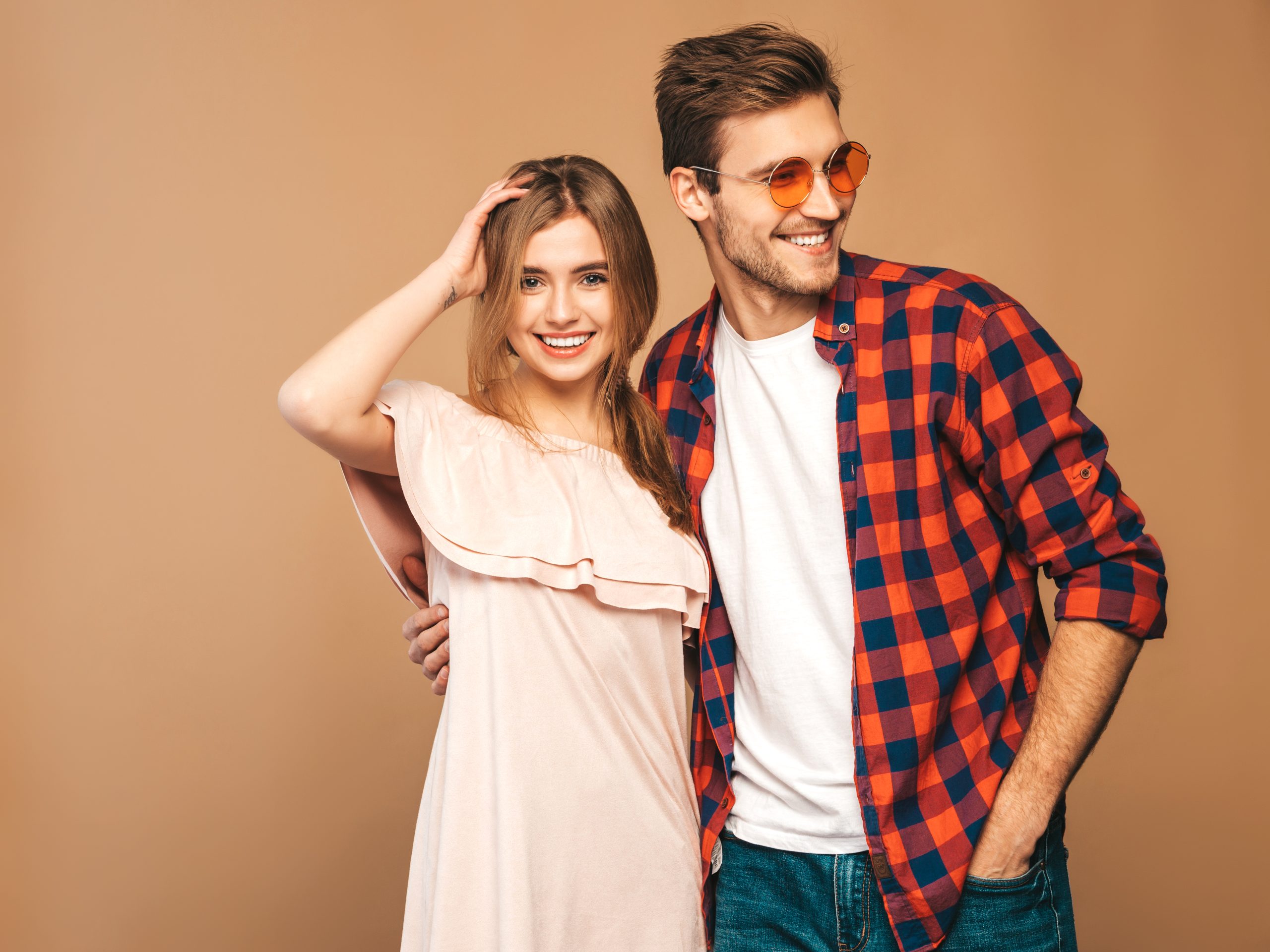 Portrait of Smiling Beautiful Girl and her Handsome Boyfriend laughing.Happy Cheerful Family. in sunglasses.Valentine's Day. Posing on beige wall. Hugging